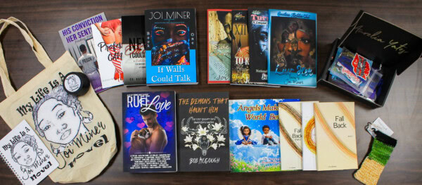 A collection of books, bookmarks, and tote bags featuring diverse authors and artwork spread out on a wooden table; items include novels, poetry, and art prints with vibrant covers.